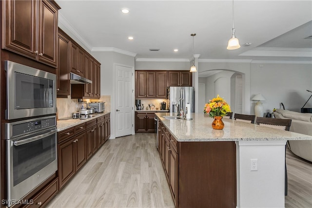 kitchen featuring decorative backsplash, appliances with stainless steel finishes, light wood-type flooring, decorative light fixtures, and a large island