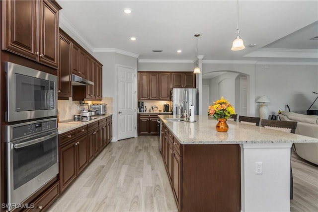 kitchen with under cabinet range hood, light wood-style floors, open floor plan, backsplash, and built in microwave