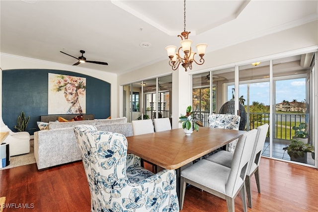 dining area with a tray ceiling, crown molding, dark wood-type flooring, and ceiling fan with notable chandelier