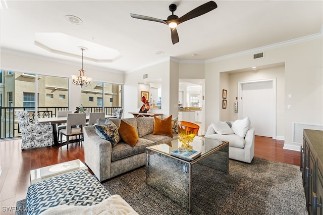 living room with ceiling fan with notable chandelier, plenty of natural light, ornamental molding, and a tray ceiling