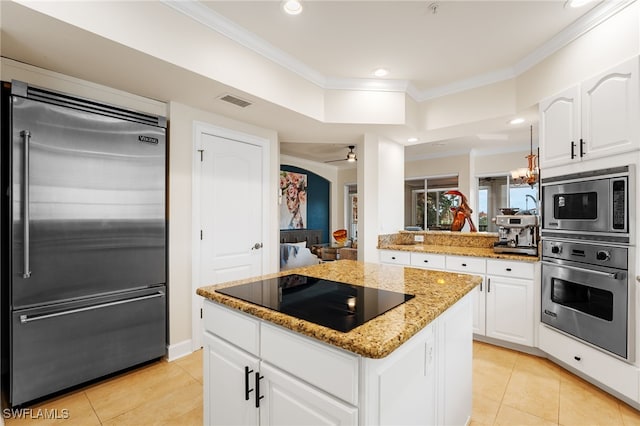 kitchen featuring white cabinets, built in appliances, ceiling fan, light stone countertops, and a kitchen island