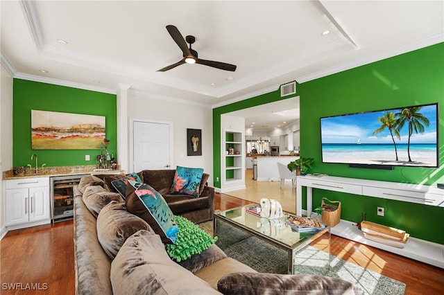 living room featuring a raised ceiling, wine cooler, built in features, hardwood / wood-style floors, and ornamental molding