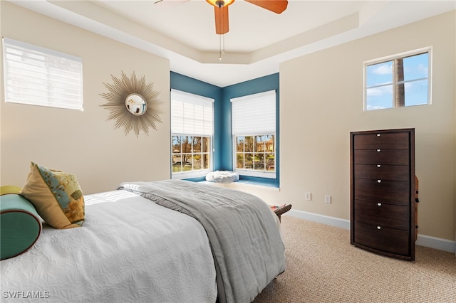 carpeted bedroom with a raised ceiling and ceiling fan