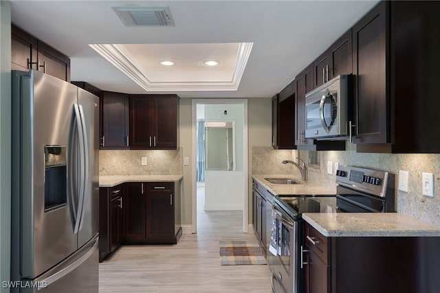 kitchen featuring dark brown cabinetry, stainless steel appliances, a tray ceiling, and sink