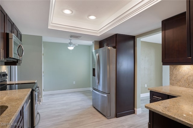 kitchen with appliances with stainless steel finishes, tasteful backsplash, light stone counters, a raised ceiling, and light hardwood / wood-style floors