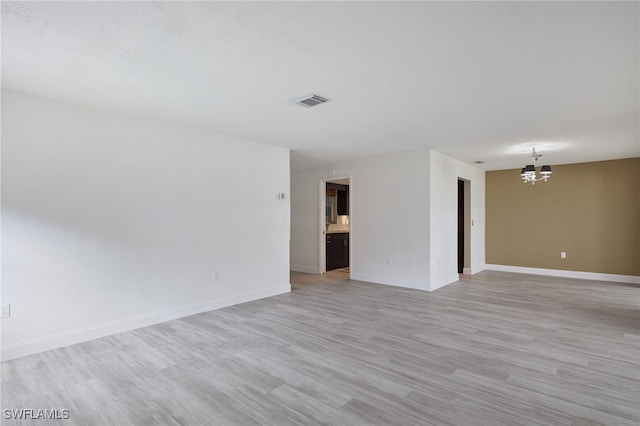 empty room featuring light wood-type flooring and a notable chandelier