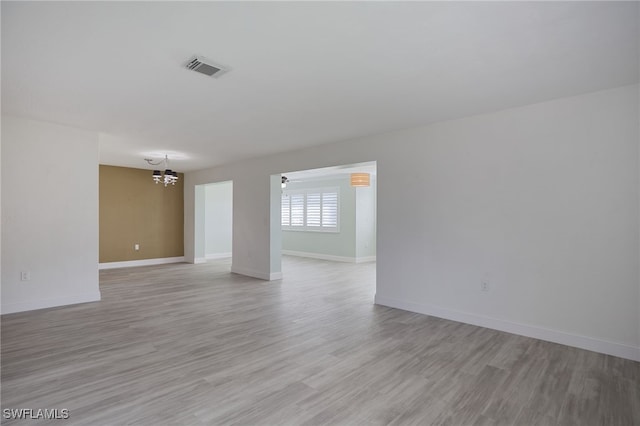 unfurnished room with ceiling fan with notable chandelier and light hardwood / wood-style floors