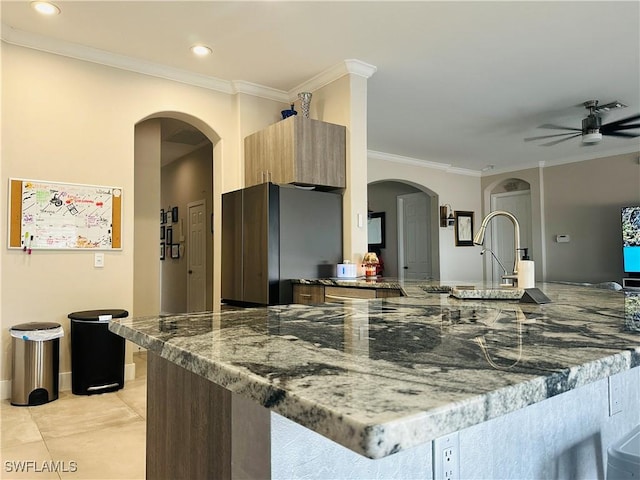 kitchen with crown molding, stainless steel fridge, kitchen peninsula, and stone counters