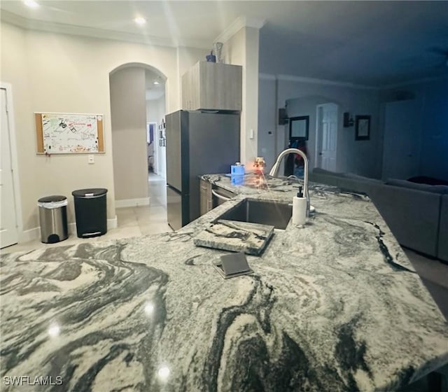 kitchen with light stone counters, ornamental molding, sink, and stainless steel refrigerator