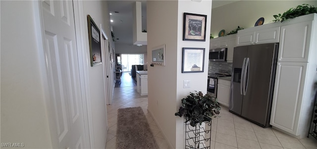 kitchen with stainless steel appliances, light tile patterned floors, tasteful backsplash, and white cabinetry