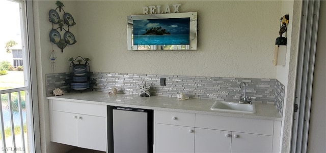 bar featuring decorative backsplash, sink, a healthy amount of sunlight, and white cabinetry