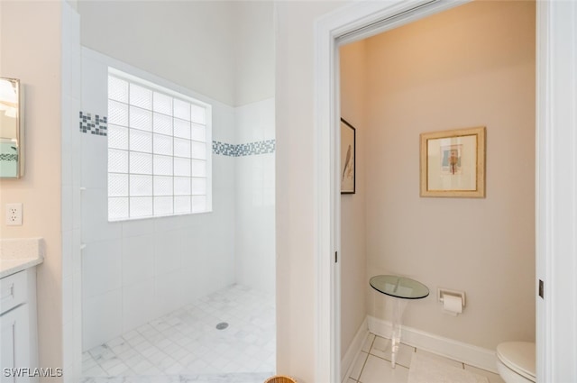 bathroom with toilet, baseboards, tiled shower, and vanity