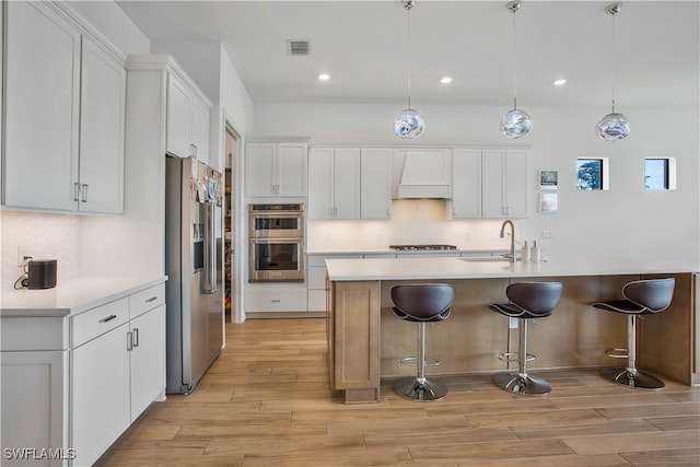 kitchen featuring white cabinets, a kitchen island with sink, stainless steel appliances, and decorative light fixtures