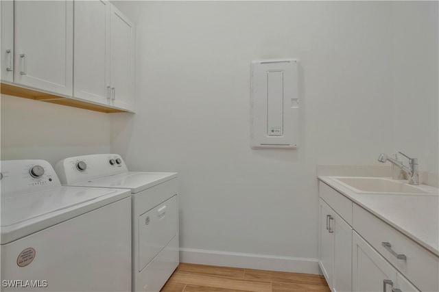 clothes washing area with sink, light wood-type flooring, washer and clothes dryer, cabinets, and electric panel