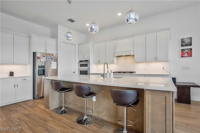 kitchen featuring custom exhaust hood, appliances with stainless steel finishes, white cabinetry, and light hardwood / wood-style floors