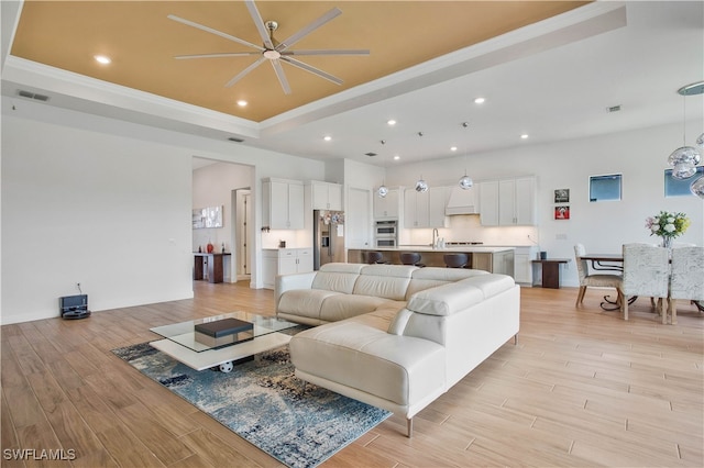 living room with ornamental molding, sink, a raised ceiling, light hardwood / wood-style floors, and ceiling fan