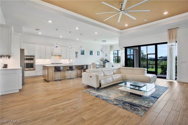 living room featuring crown molding, ceiling fan, a raised ceiling, and light wood-type flooring