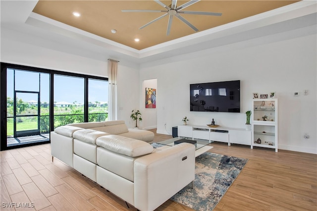 living room featuring a high ceiling, a tray ceiling, light wood-type flooring, and ceiling fan