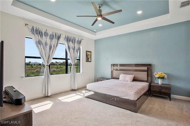 carpeted bedroom with ceiling fan and a raised ceiling