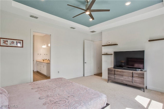 carpeted bedroom featuring ensuite bathroom, a raised ceiling, and ceiling fan