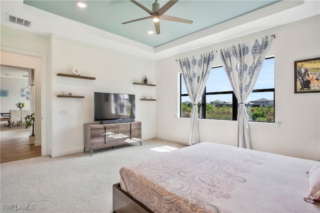 carpeted bedroom with a raised ceiling and ceiling fan