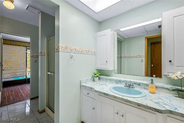 bathroom featuring tile patterned flooring, vanity, walk in shower, and a paneled ceiling