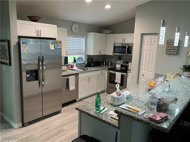 kitchen with white cabinets, appliances with stainless steel finishes, dark stone countertops, light wood-type flooring, and vaulted ceiling