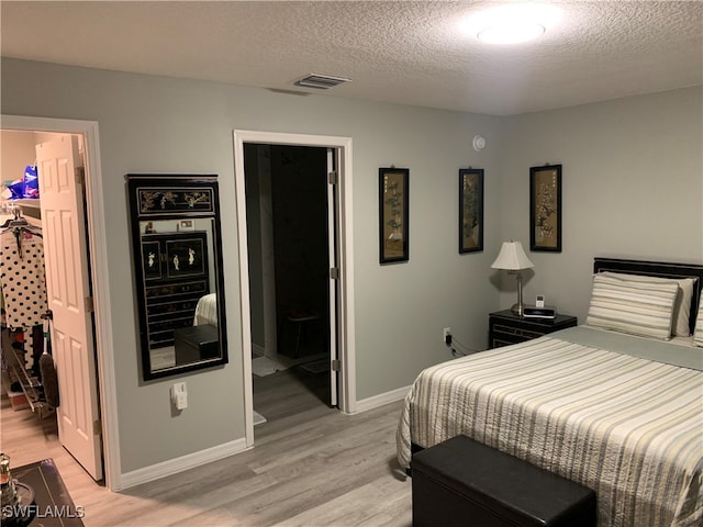 bedroom with a spacious closet, light hardwood / wood-style floors, and a textured ceiling