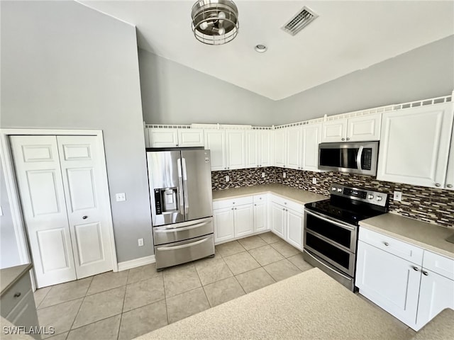 kitchen featuring decorative backsplash, white cabinets, light tile patterned flooring, vaulted ceiling, and appliances with stainless steel finishes