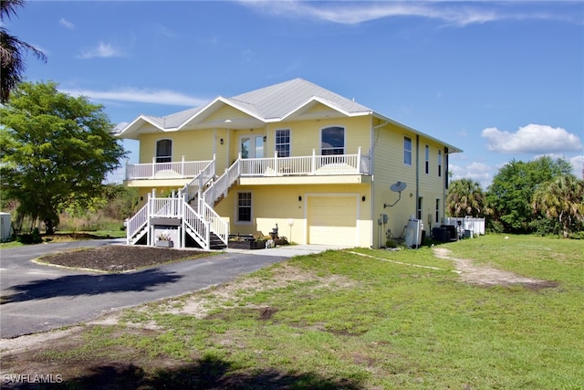 raised beach house featuring cooling unit, covered porch, a front yard, and a garage