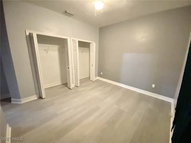 unfurnished bedroom featuring multiple closets and light hardwood / wood-style floors