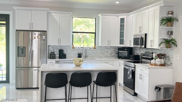 kitchen with white cabinets, tasteful backsplash, a breakfast bar, ornamental molding, and stainless steel appliances