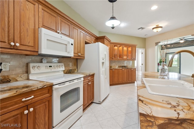 kitchen featuring light stone countertops, hanging light fixtures, decorative backsplash, sink, and white appliances