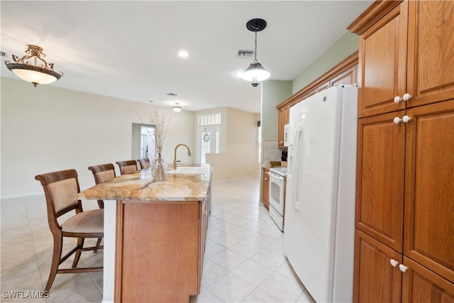 kitchen with a kitchen bar, a center island with sink, sink, light stone countertops, and white appliances