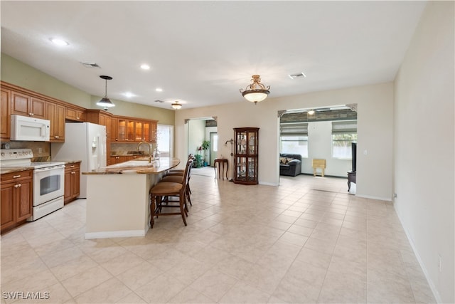 kitchen featuring hanging light fixtures, a breakfast bar area, tasteful backsplash, a kitchen island with sink, and white appliances