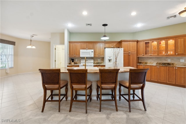 kitchen featuring a breakfast bar, tasteful backsplash, decorative light fixtures, an island with sink, and white appliances