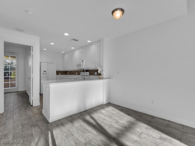 kitchen with light wood-type flooring, kitchen peninsula, white appliances, and white cabinetry