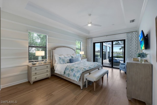 bedroom with ceiling fan, access to outside, a tray ceiling, light wood-type flooring, and ornamental molding