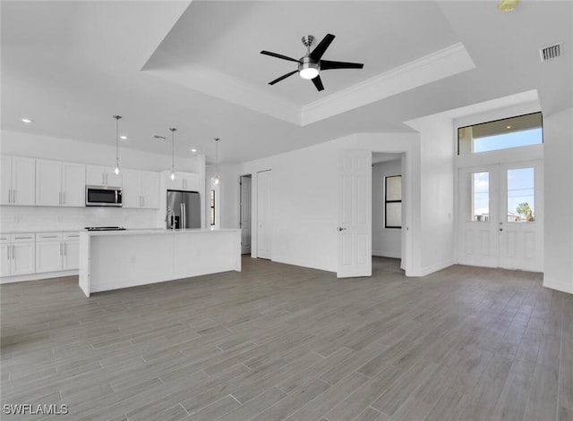 unfurnished living room with ceiling fan, a tray ceiling, light wood-type flooring, and ornamental molding