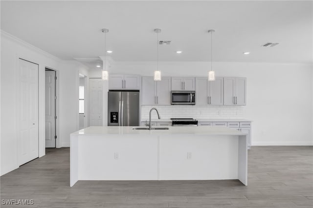 kitchen with an island with sink, hanging light fixtures, sink, and stainless steel appliances