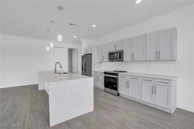 kitchen featuring an island with sink, decorative light fixtures, stainless steel appliances, light hardwood / wood-style floors, and decorative backsplash