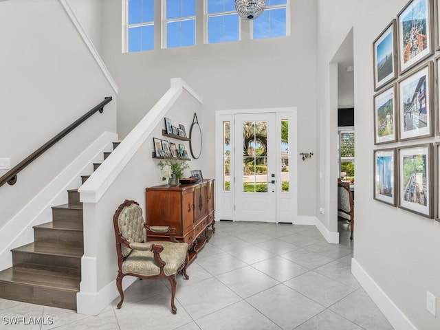 tiled entryway featuring a towering ceiling, stairs, and baseboards