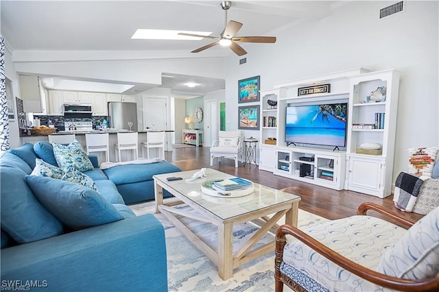 living room with ceiling fan, vaulted ceiling with skylight, and dark hardwood / wood-style floors