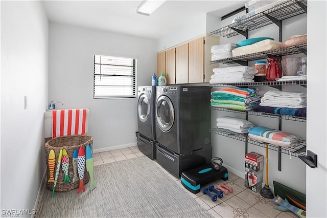 clothes washing area with cabinets, washing machine and clothes dryer, and light tile patterned floors