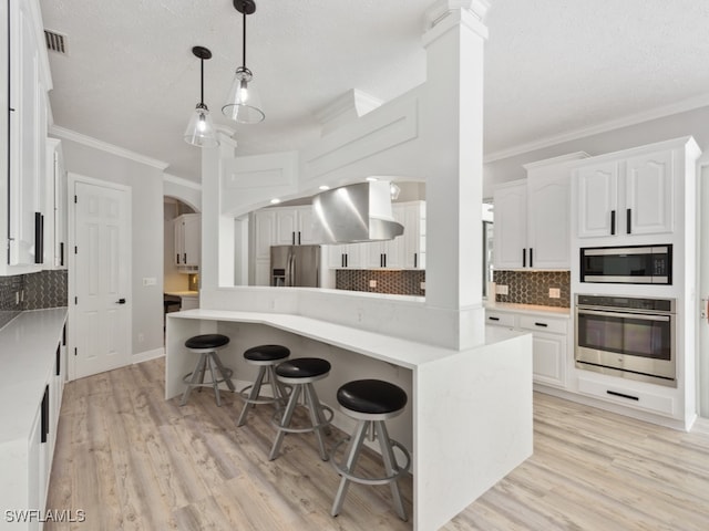 kitchen with wall chimney exhaust hood, crown molding, light hardwood / wood-style flooring, stainless steel appliances, and white cabinetry