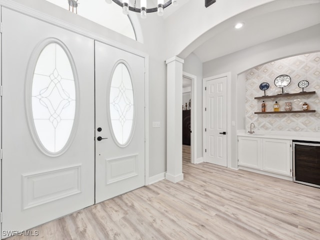 entrance foyer featuring ornate columns, light wood-type flooring, beverage cooler, and sink