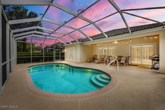 pool at dusk featuring a patio, glass enclosure, and ceiling fan