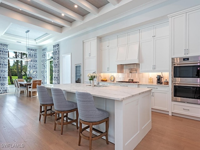 kitchen with light hardwood / wood-style flooring, white cabinetry, a kitchen island with sink, and stainless steel appliances