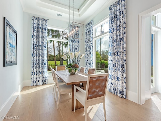 dining area featuring a chandelier, light hardwood / wood-style floors, and a raised ceiling