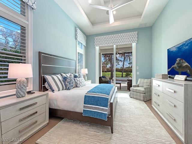 bedroom featuring multiple windows, access to exterior, a tray ceiling, and ceiling fan